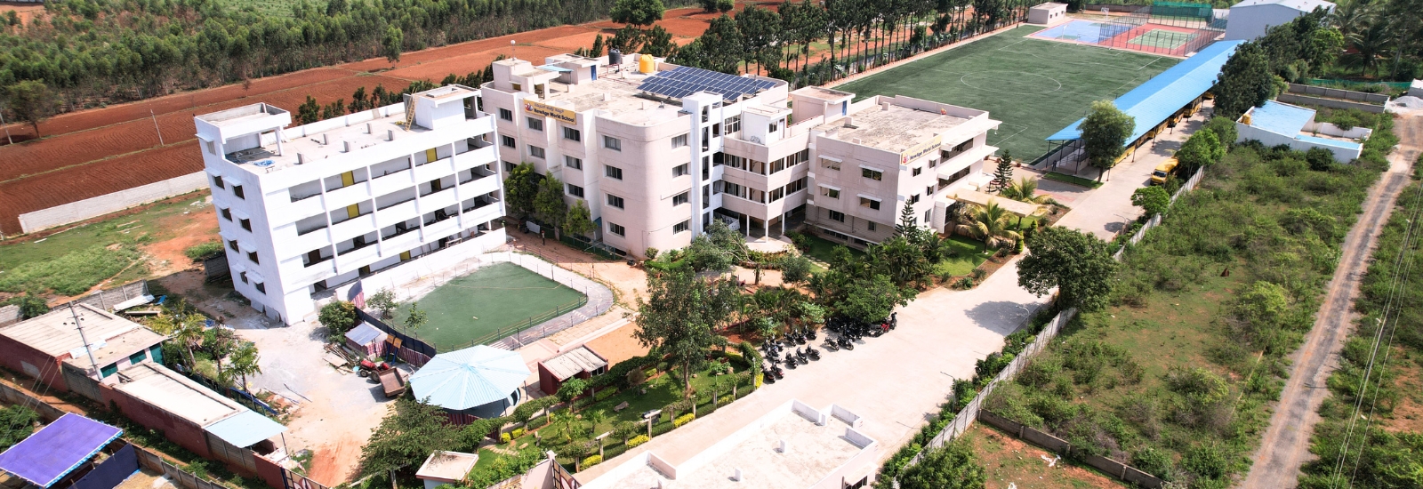 NewAge World School Yelahanka campus showcasing buildings, playgrounds, and greenery, highlighting its infrastructure and facilities.